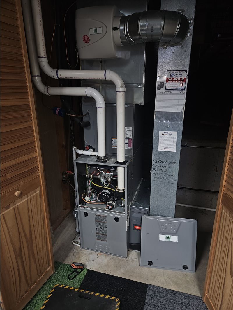 Furnace and humidifier system in a utility closet. Gray metal, white pipes, and wood doors.
