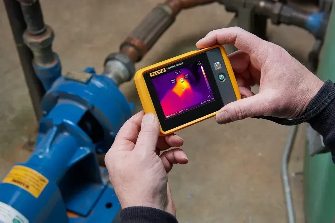Person using thermal imaging camera on blue pump, detecting heat.