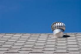 Metallic roof vent on a gray shingled roof against a bright blue sky.