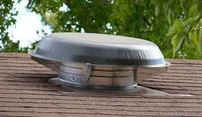 A metal roof vent on a brown shingled roof against a backdrop of green trees.