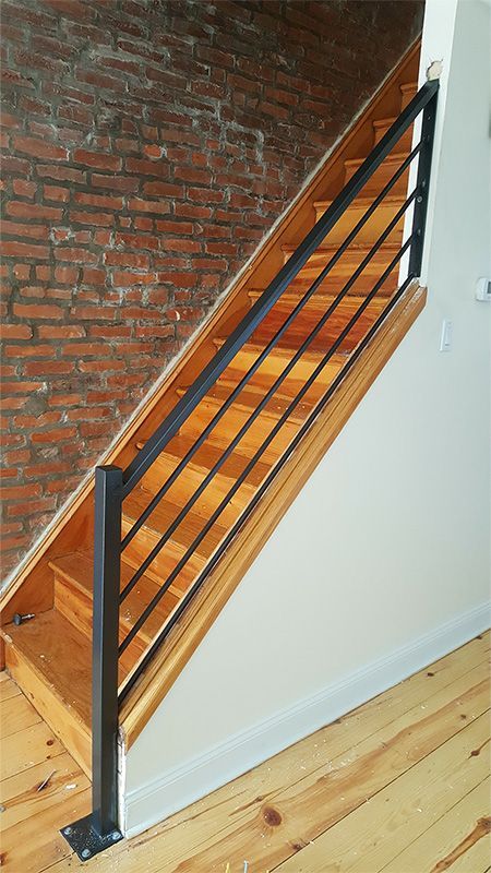 A wooden staircase with a metal railing in front of a brick wall.