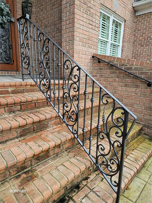 There is a wrought iron railing on the stairs of a brick house.