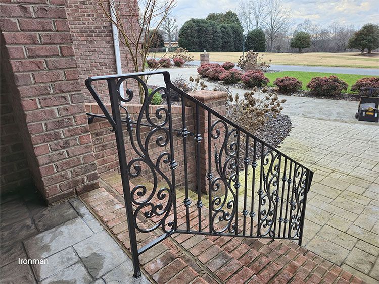 A wrought iron railing is sitting on a brick porch next to a brick building.