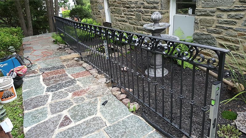 A wrought iron fence is being built in front of a stone building.
