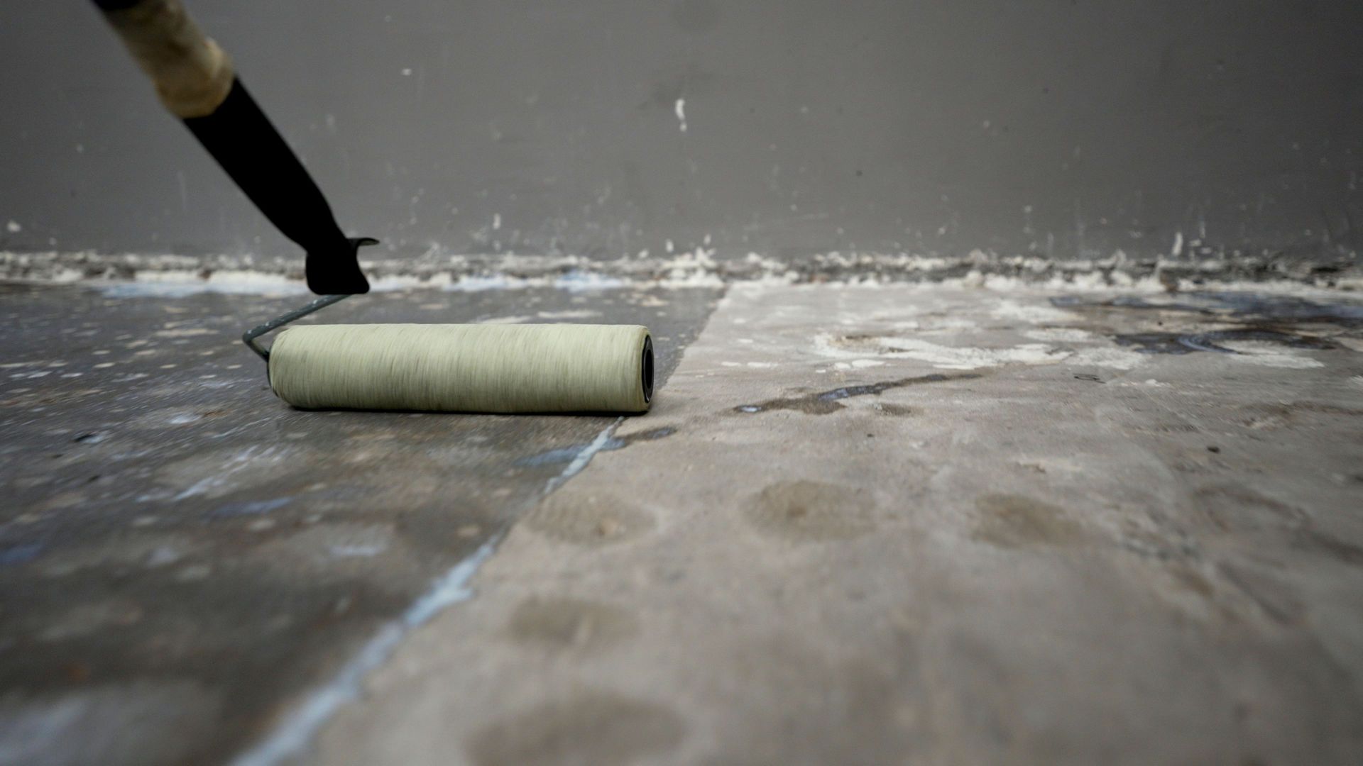 Worker applying waterproofing membrane to concrete floor using paint roller.