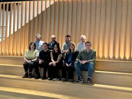 A group of people are posing for a picture in front of a wooden wall.