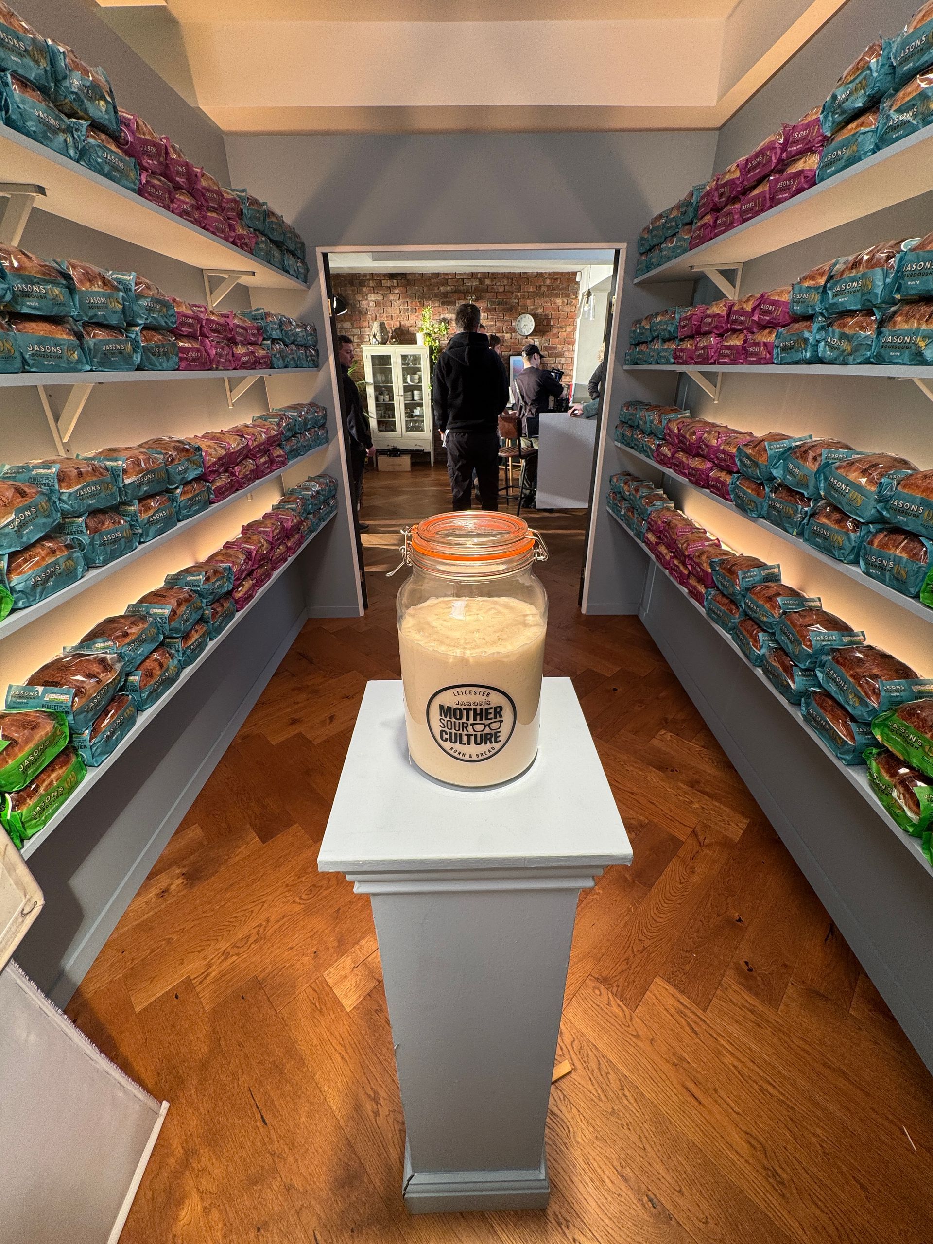 Jar on pedestal in shop aisle with stacked product on shelves.