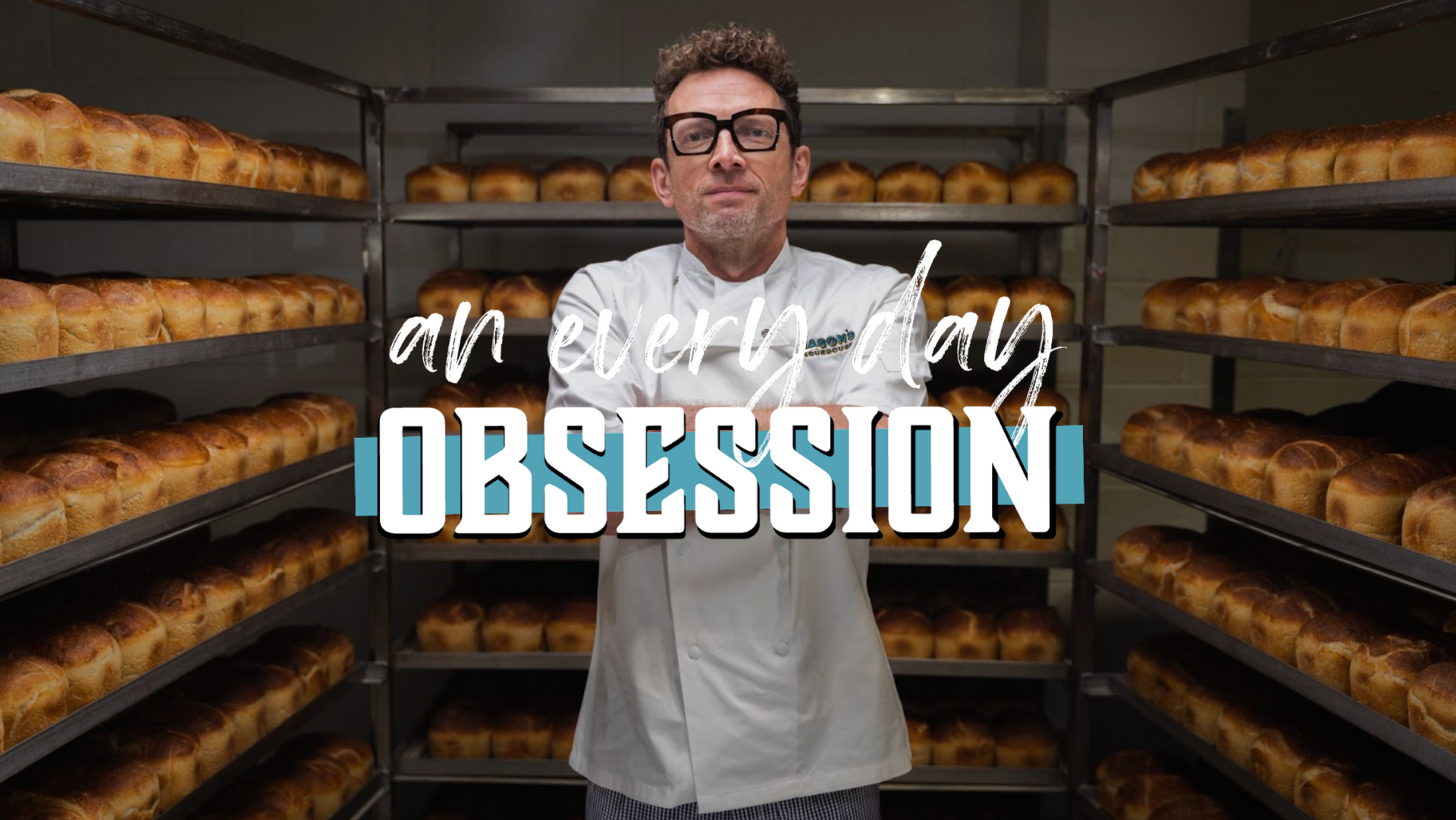 A man is standing in front of a rack of bread in a bakery.