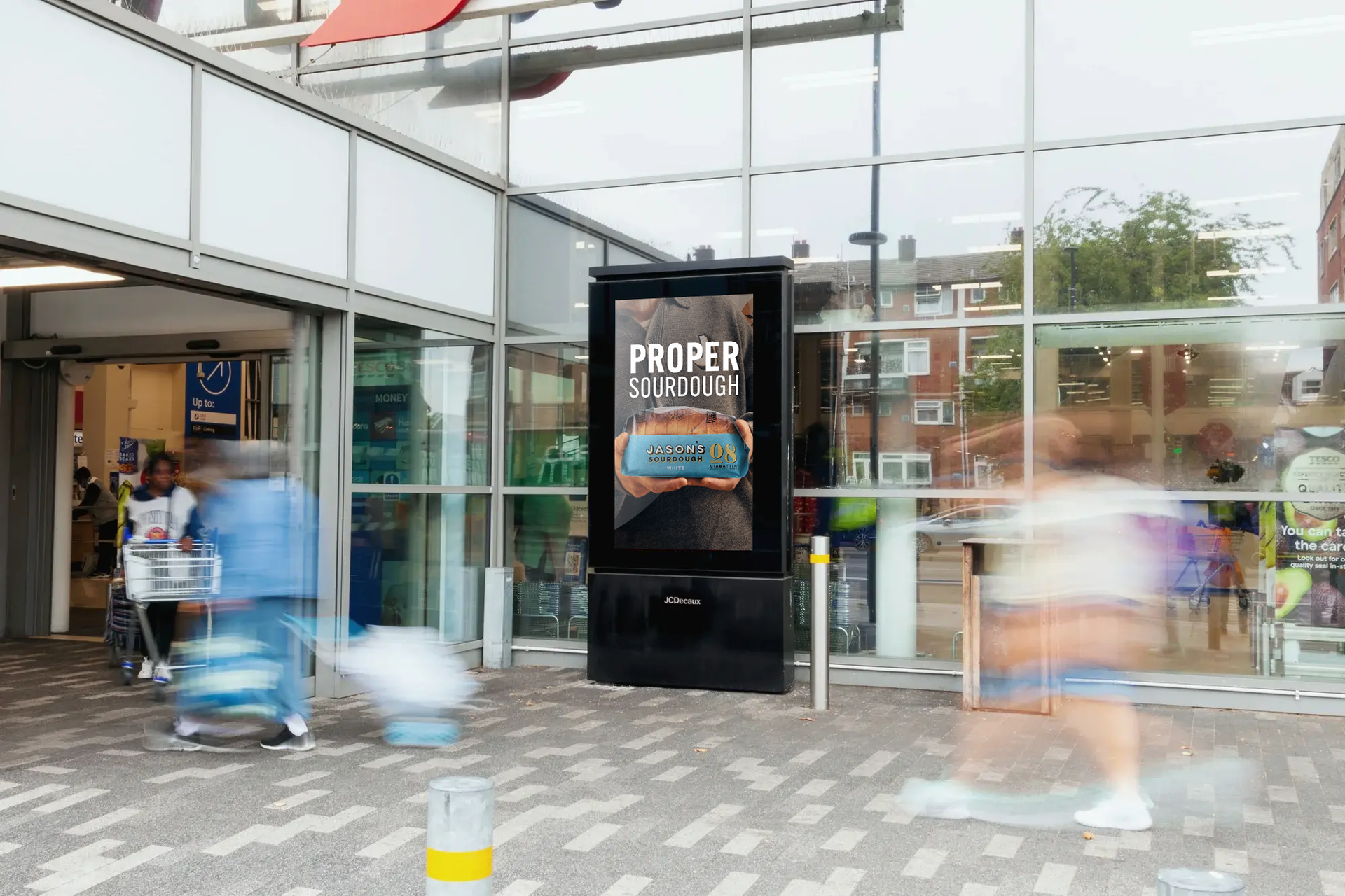 Digital sign outside of store with blurred figures walking by. Sign displays a car advertisement.