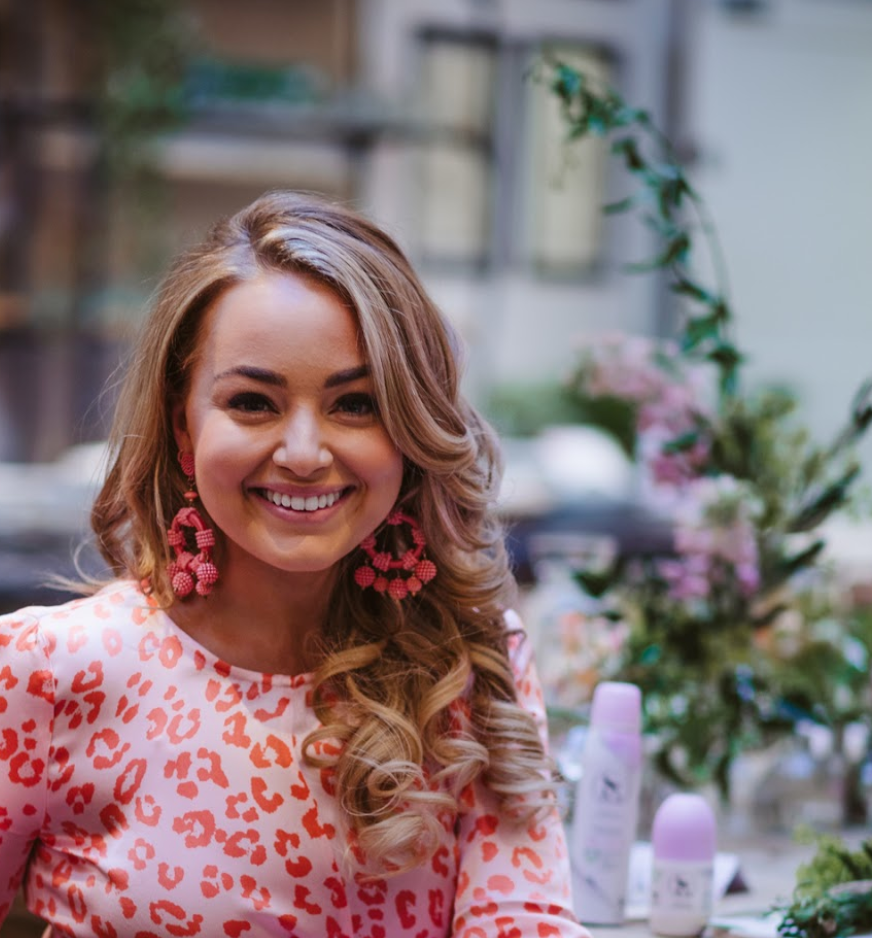A woman wearing a pink leopard print shirt and pink earrings is smiling.