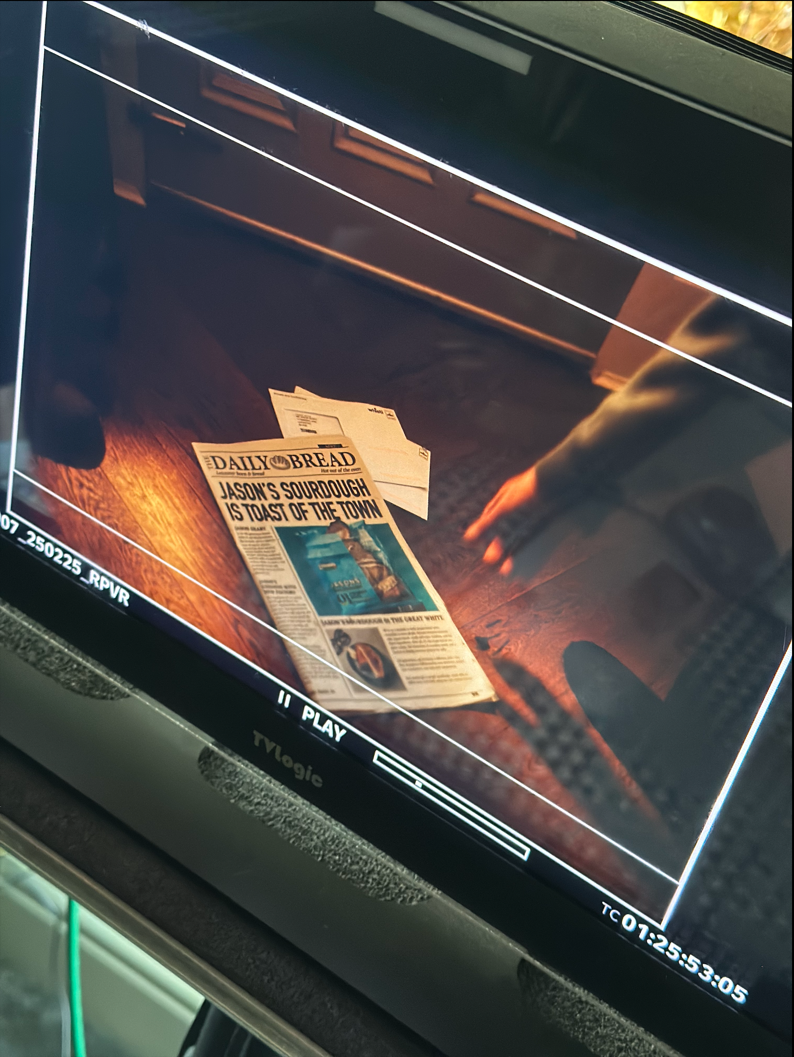 Newspaper and tickets on a table, a hand reaching towards them, viewed from a monitor.