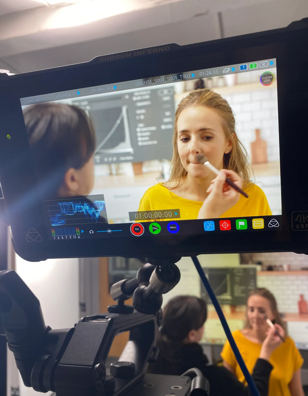A woman is applying makeup to another woman in front of a camera