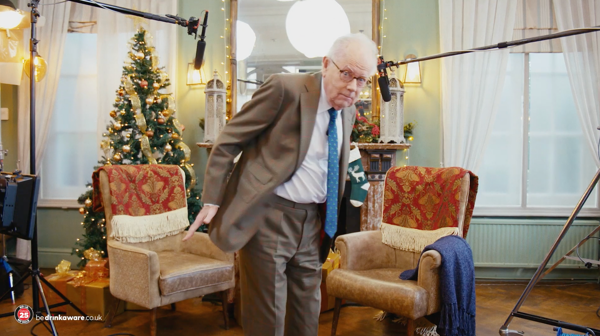 A man in a suit and tie is standing in front of a christmas tree in a living room.