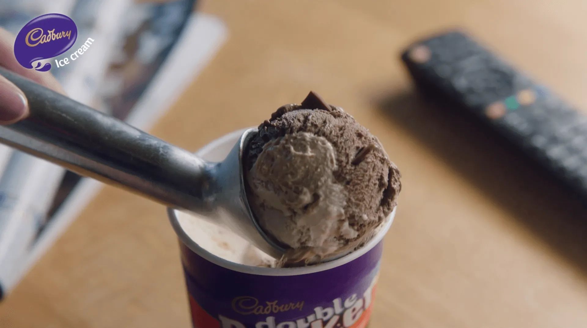 A person is scooping ice cream out of a cup next to a remote control.