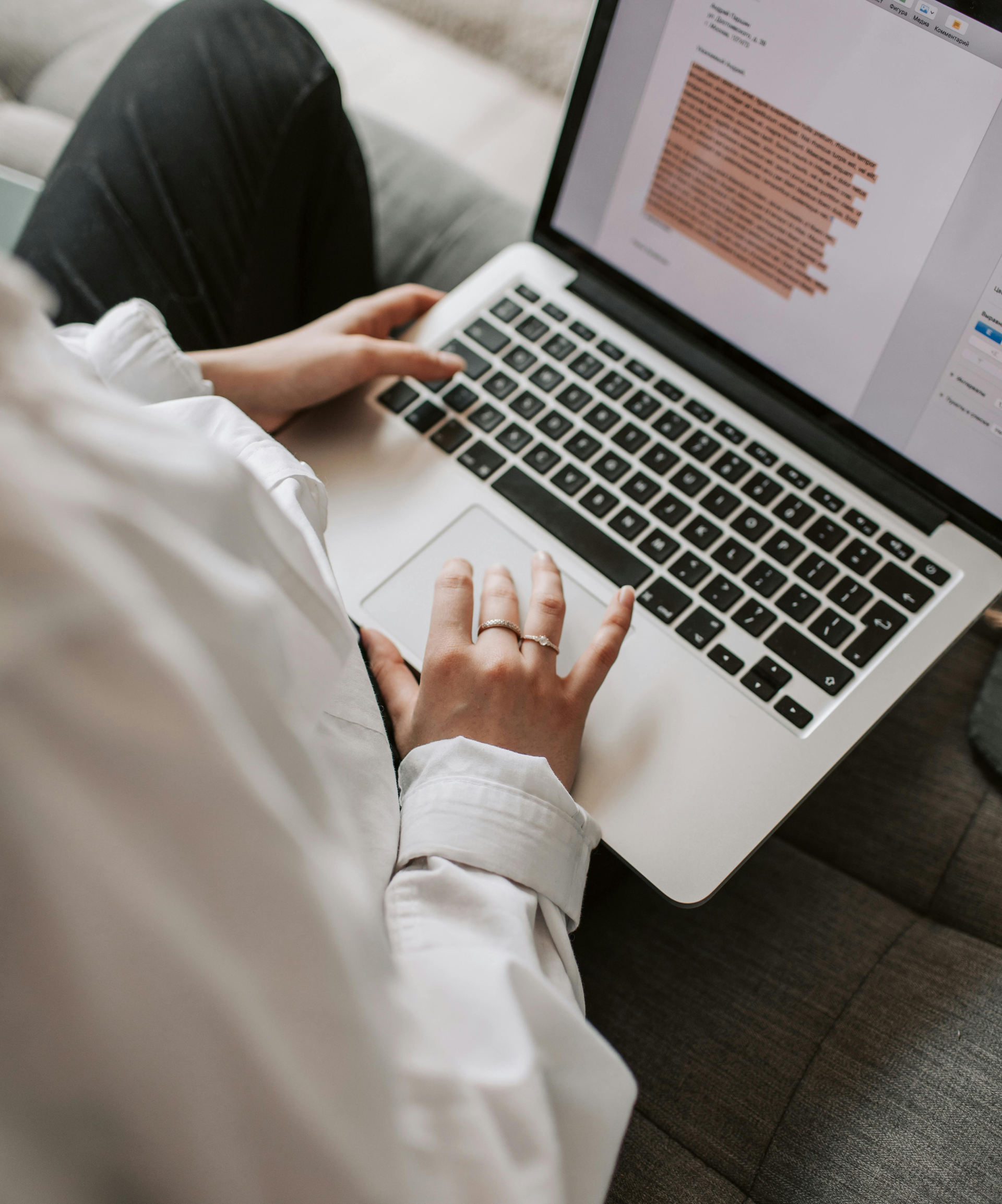 A person is typing on a laptop with a ring on their finger