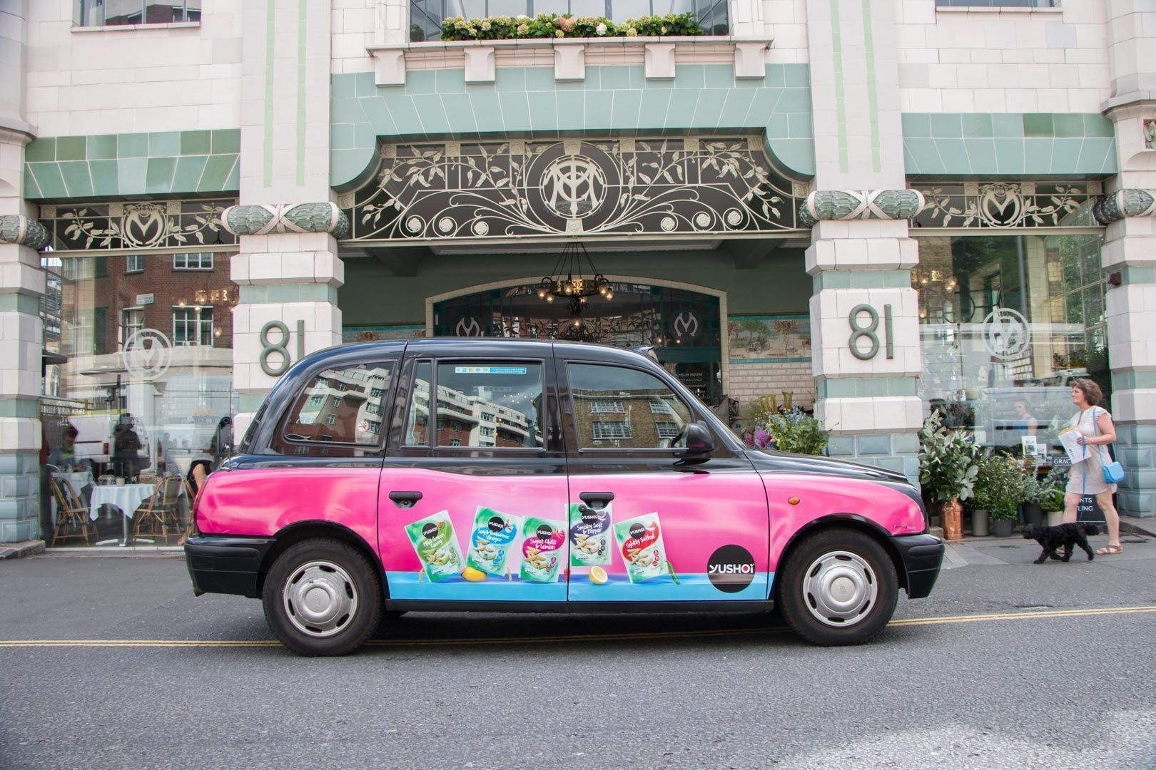 A pink and black taxi cab is parked in front of a building.