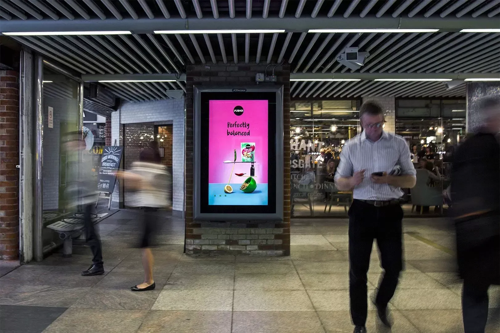 A man is looking at his phone while walking in front of a sign.