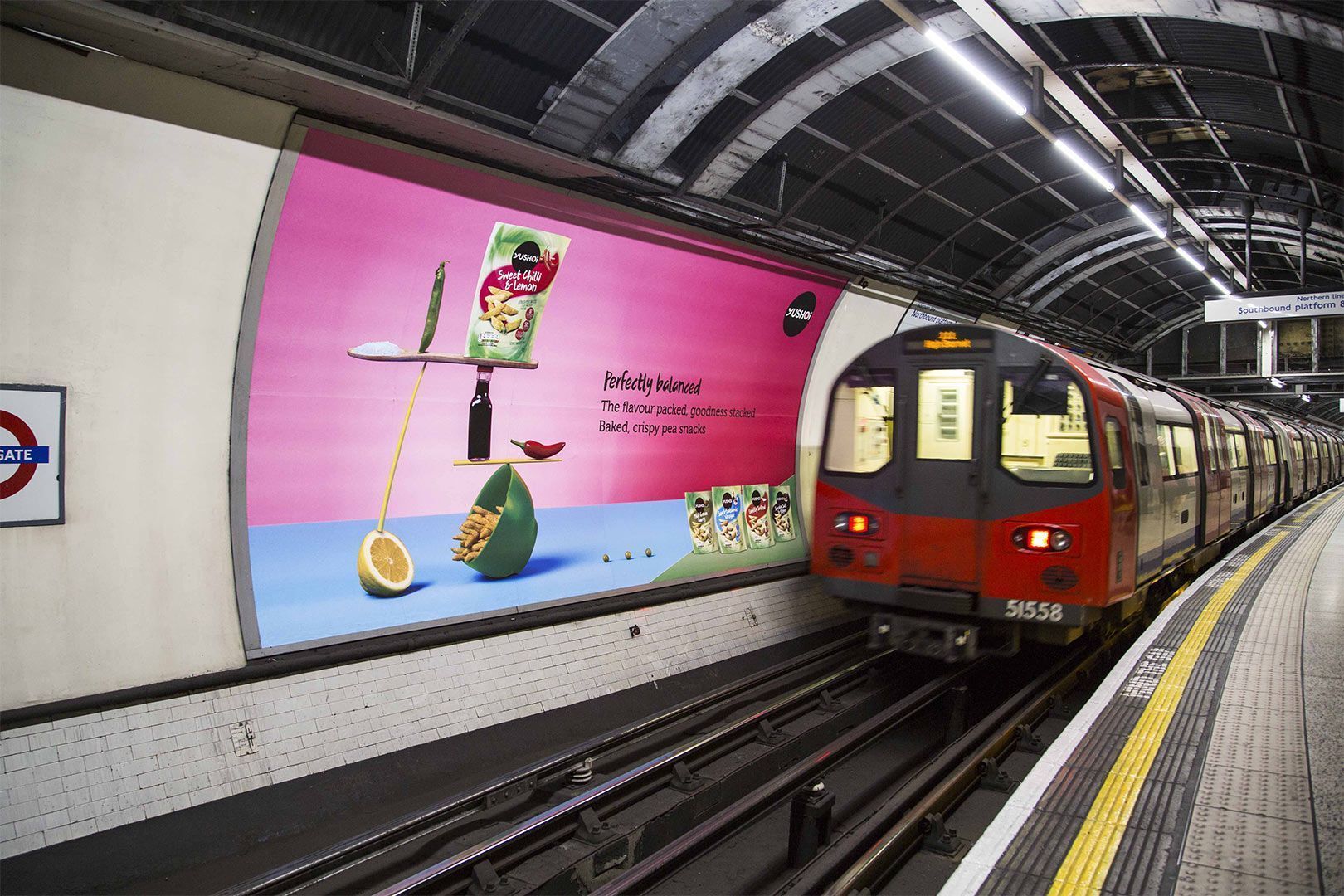 A train is pulling into a subway station with a large billboard on the wall.