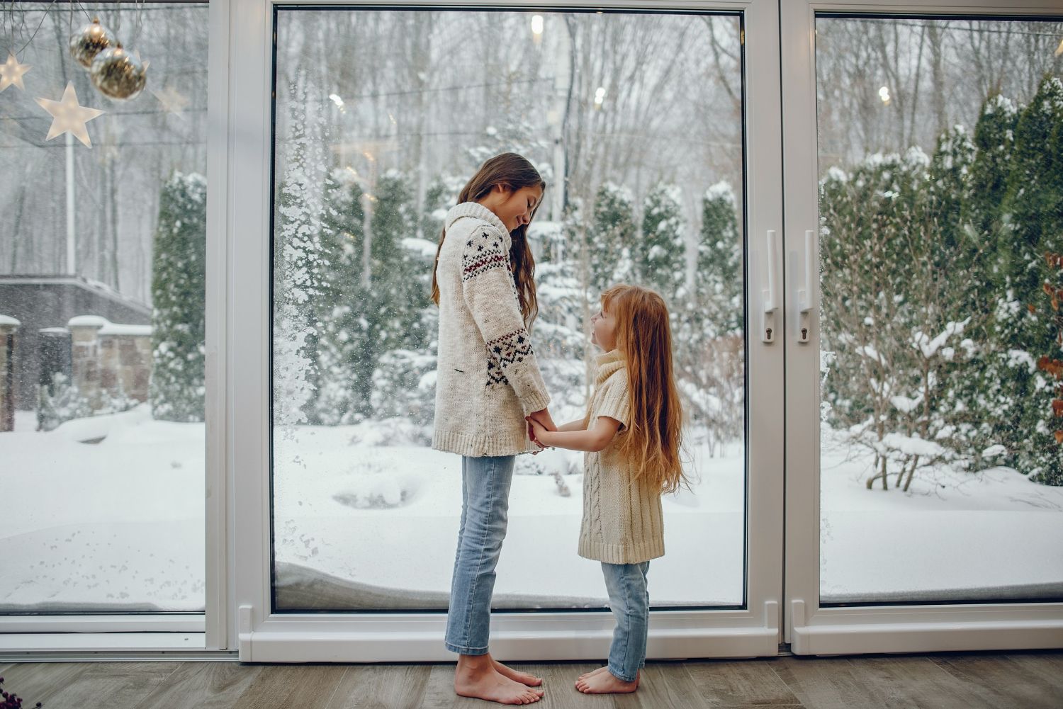 Woman and girl hold hands, standing in front of a snowy window.