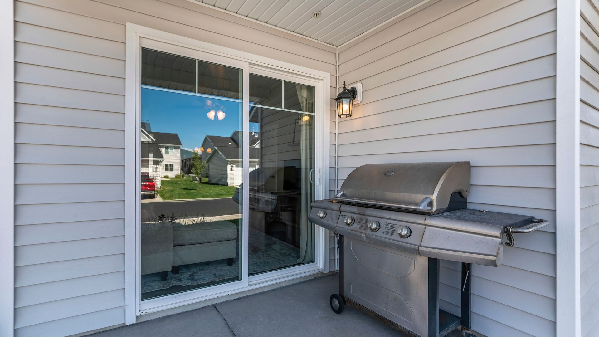 Sliding glass door opens onto a patio with a gas grill. The house is light grey.