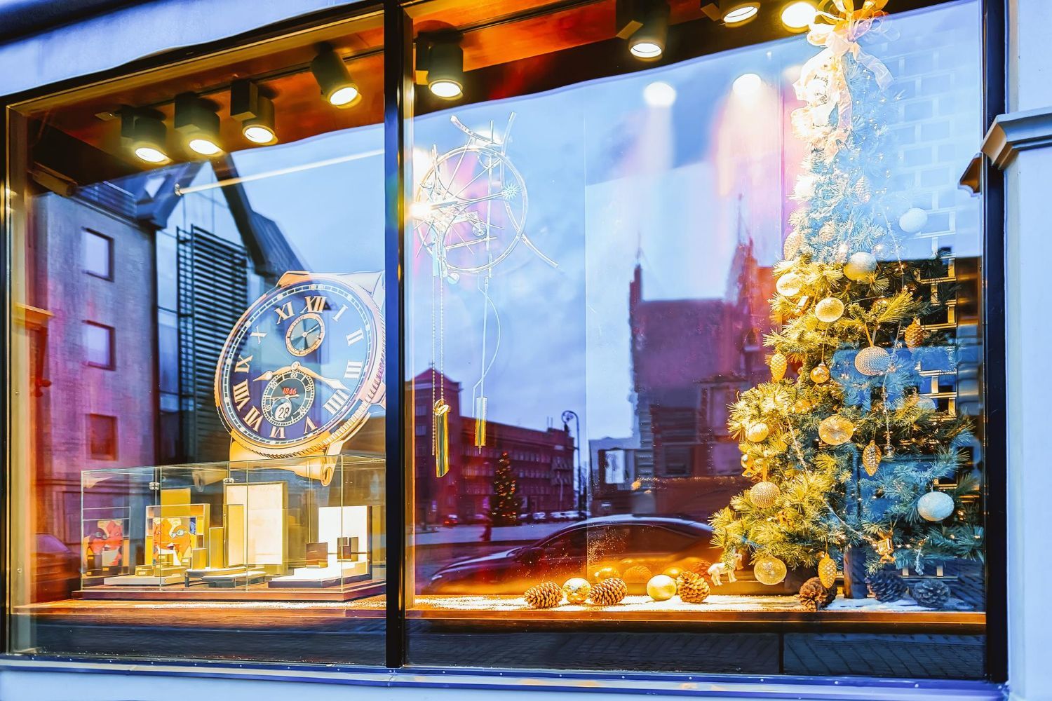 A jewelry store window displays a watch and a decorated Christmas tree with the city street visible in the reflection.