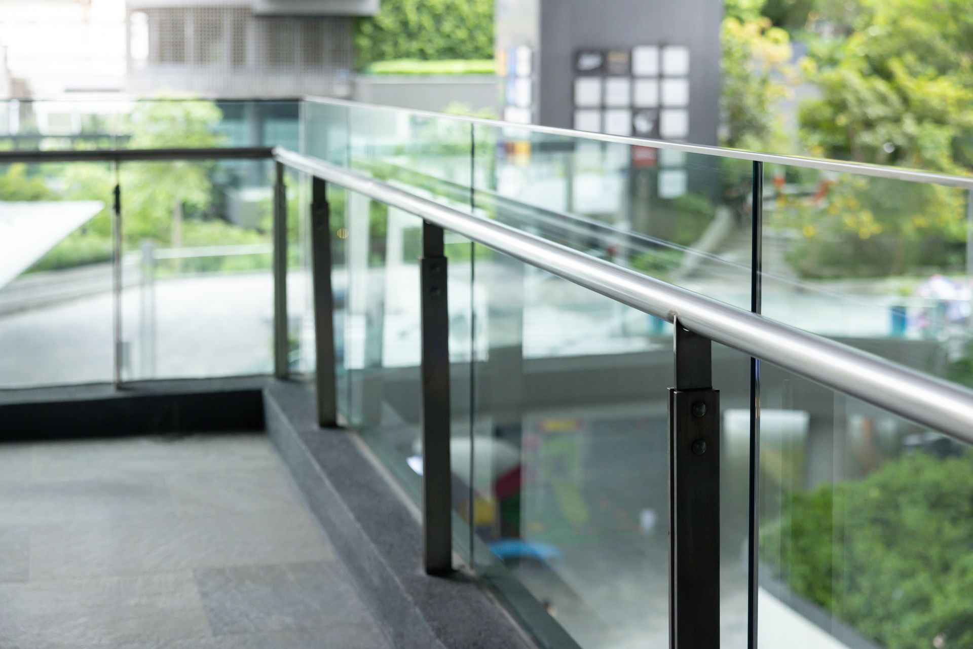 Glass and metal railing on a balcony overlooking a blurred green outdoor setting.
