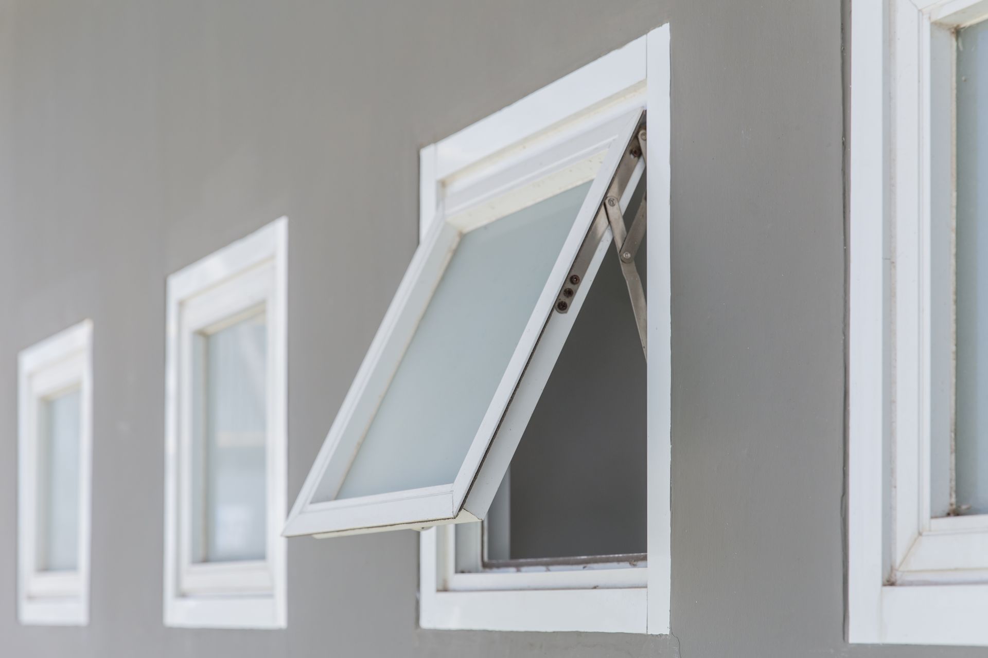 A row of small windows on a gray wall, with one window open outward.