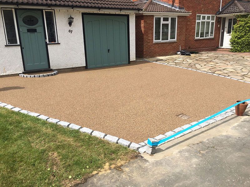 Brown resin driveway in front of green doors, with block paving border