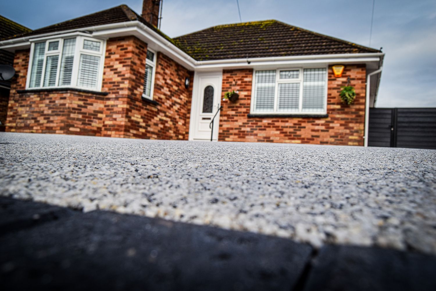 Grey resin driveway with a red brick home in the background