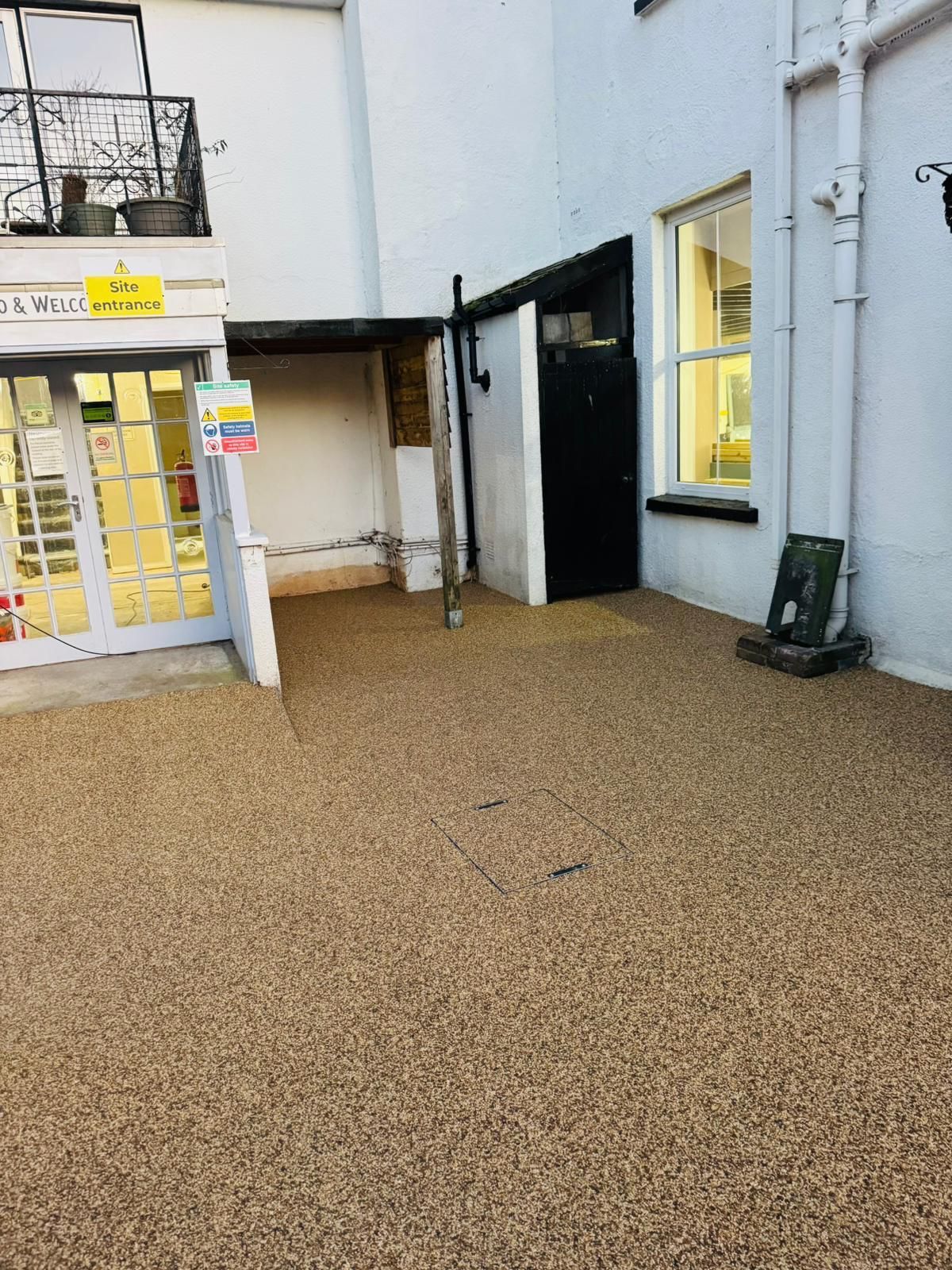 Gravel-covered outdoor area next to a white building with a black door and a window.