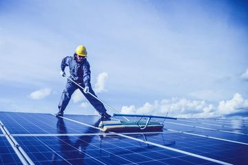 A man is cleaning a solar panel with a broom.