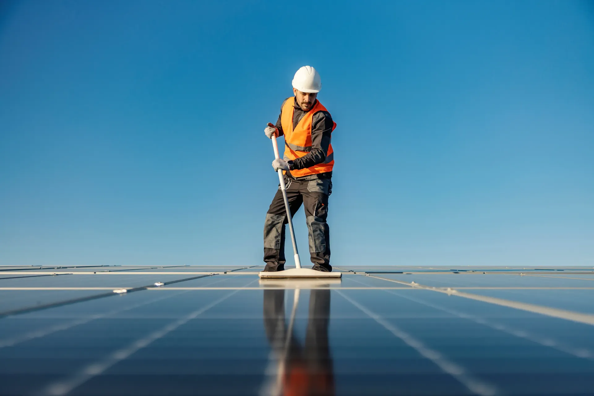 A man is cleaning a solar panel roof with a mop.