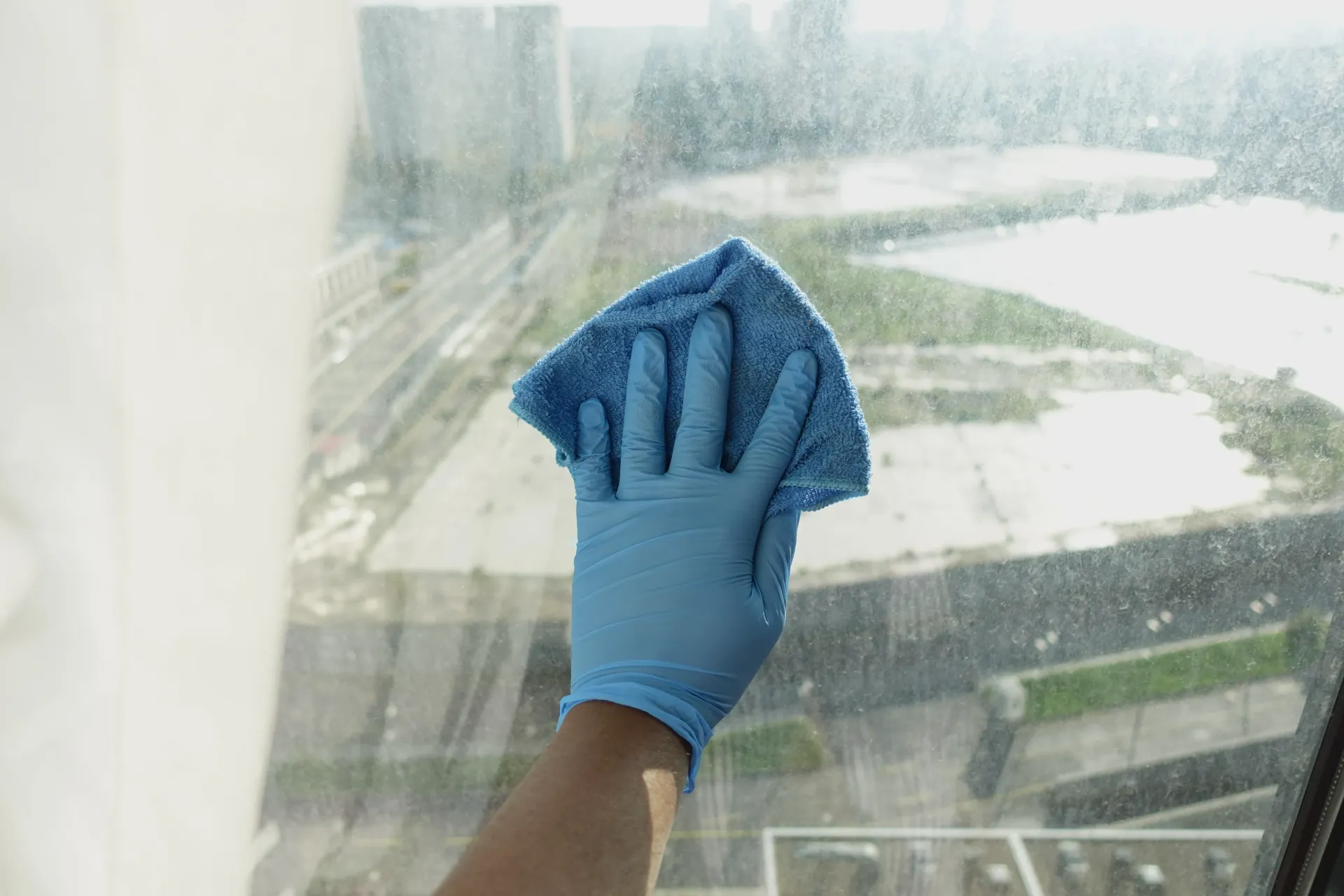 A person wearing blue gloves is cleaning a window with a cloth.