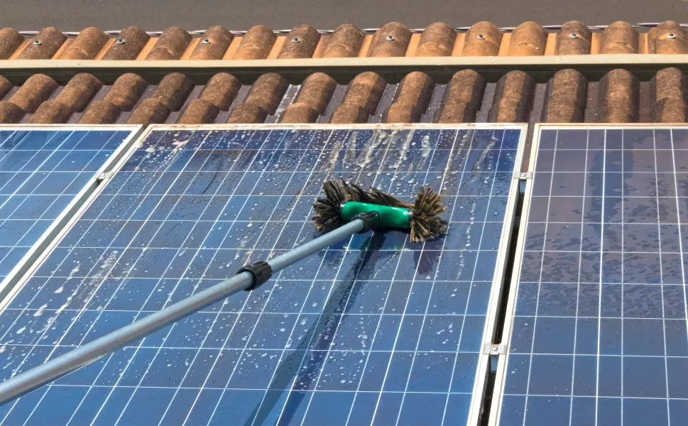 A person is cleaning a solar panel with a green brush