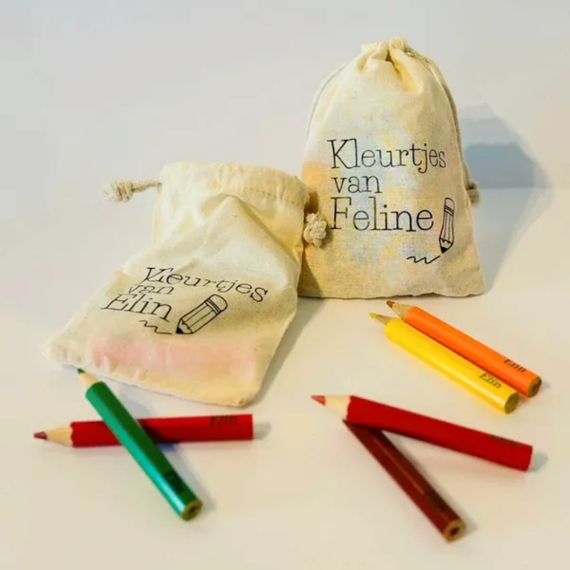 Twee stoffen cadeauzakjes met Nederlandse tekst, omringd door kleurrijke kleurpotloden op een witte achtergrond.