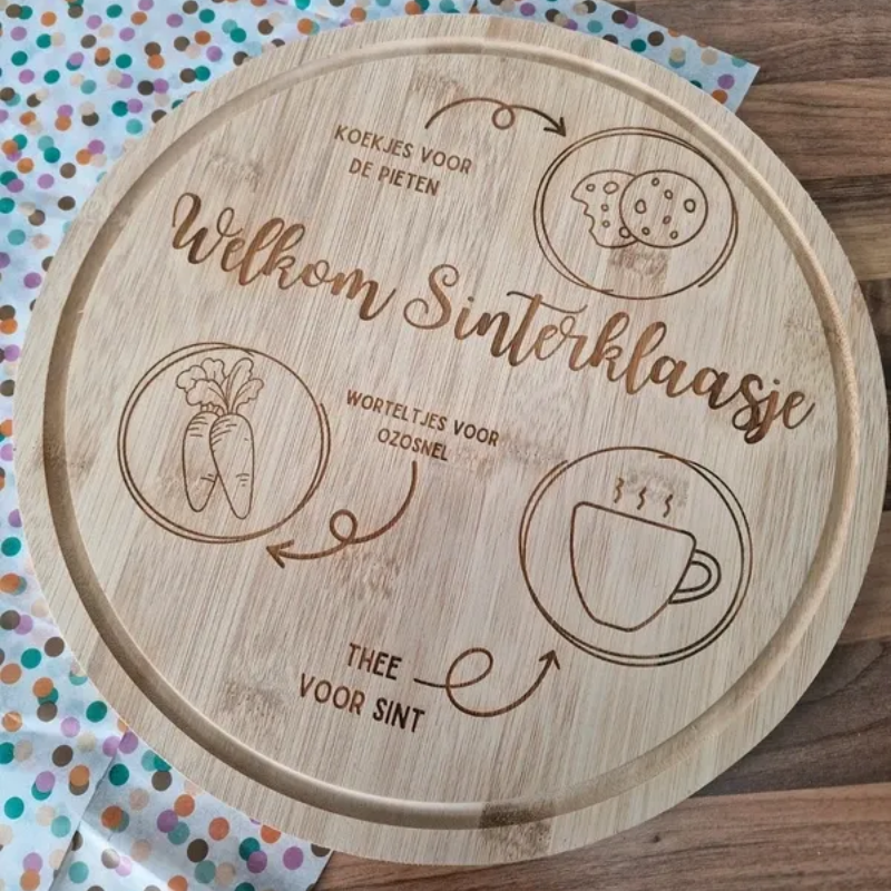 Houten Sinterklaasdienblad met gegraveerde Nederlandse etiketten voor koekjes, melk, snoep en thee op een gestippelde stoffen tafelkleed.