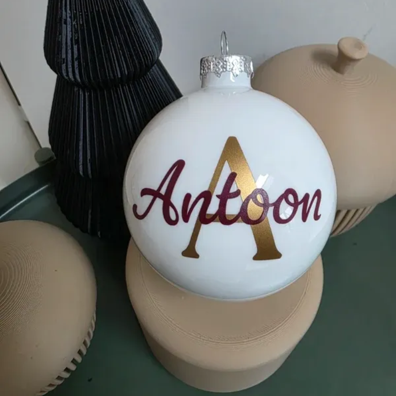 Witte kerstversiering met een gouden A en bordeauxrode tekst 