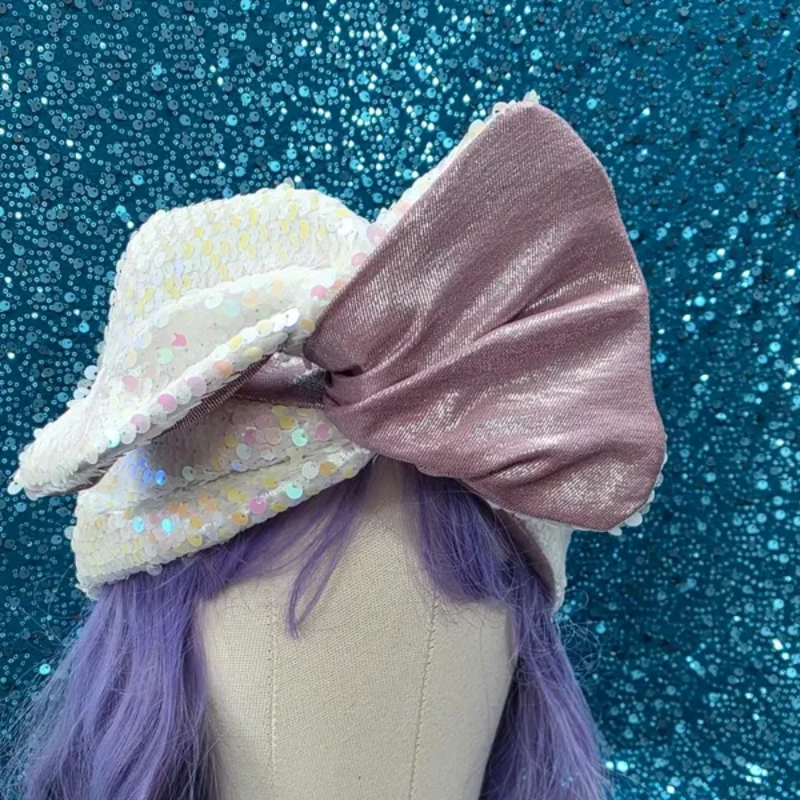 Pastelkleurige strik op een mannequin, met roze satijn, witte iriserende stof en paars haar tegen een achtergrond van blauwe glitter.