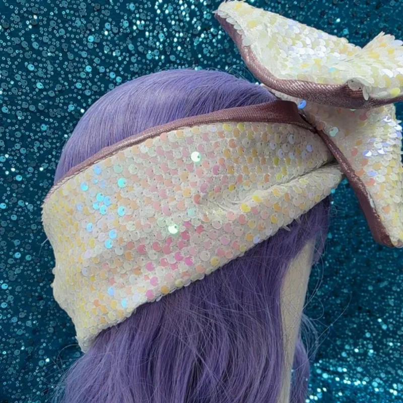 Pastelkleurige strik op een mannequin, met roze satijn, witte iriserende stof en paars haar tegen een achtergrond van blauwe glitter.
