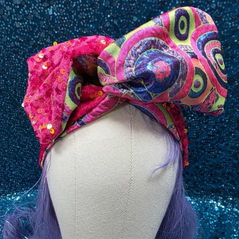 Een kleurrijke, gedessineerde tulband op een paspophoofd tegen een glinsterende blauwe achtergrond.