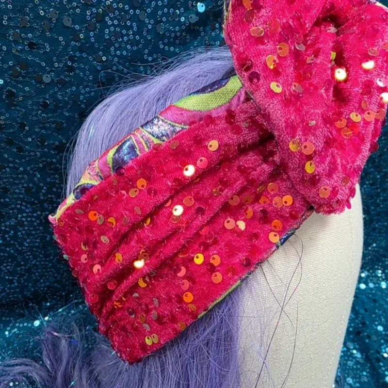 Een kleurrijke, gedessineerde tulband op een paspophoofd tegen een glinsterende blauwe achtergrond.