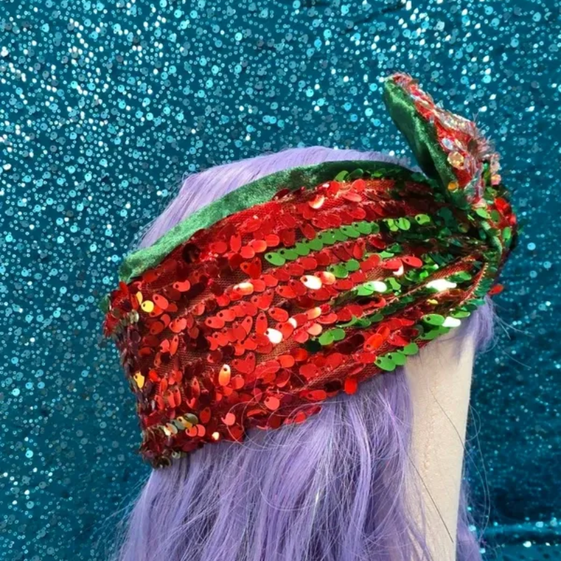 Een glinsterende rode, groene en zilveren paillettenturban op een paspophoofd tegen een blauwe glitterachtergrond.