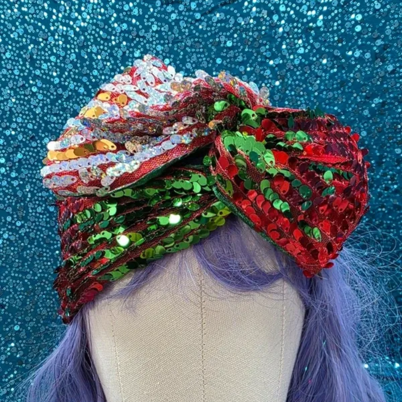 Een glinsterende rode, groene en zilveren paillettenturban op een paspophoofd tegen een blauwe glitterachtergrond.