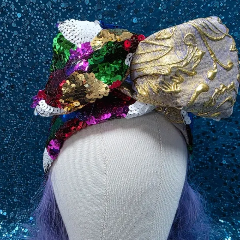 Mannequinhoofd met een kleurrijke paillettenstrik en een zilverkleurige, met goud geborduurde strik op een blauwe glitterachtergrond.