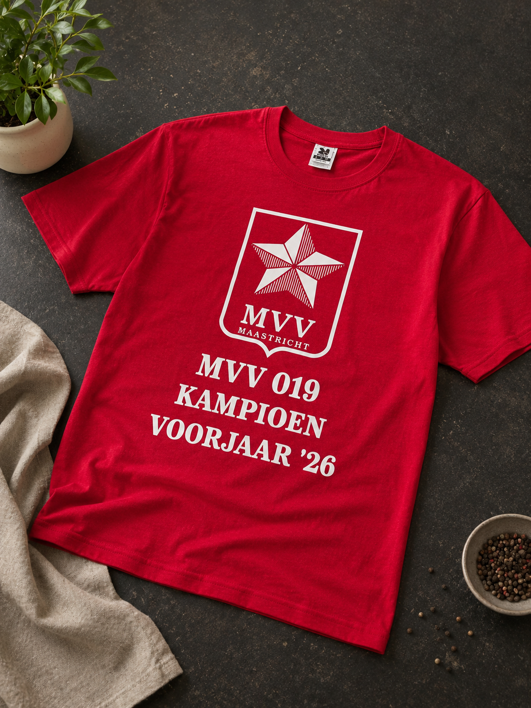 Red T-shirt with white MVV 019 KAMPIOEN VOORJAAR ’26 print, laid on a dark surface.