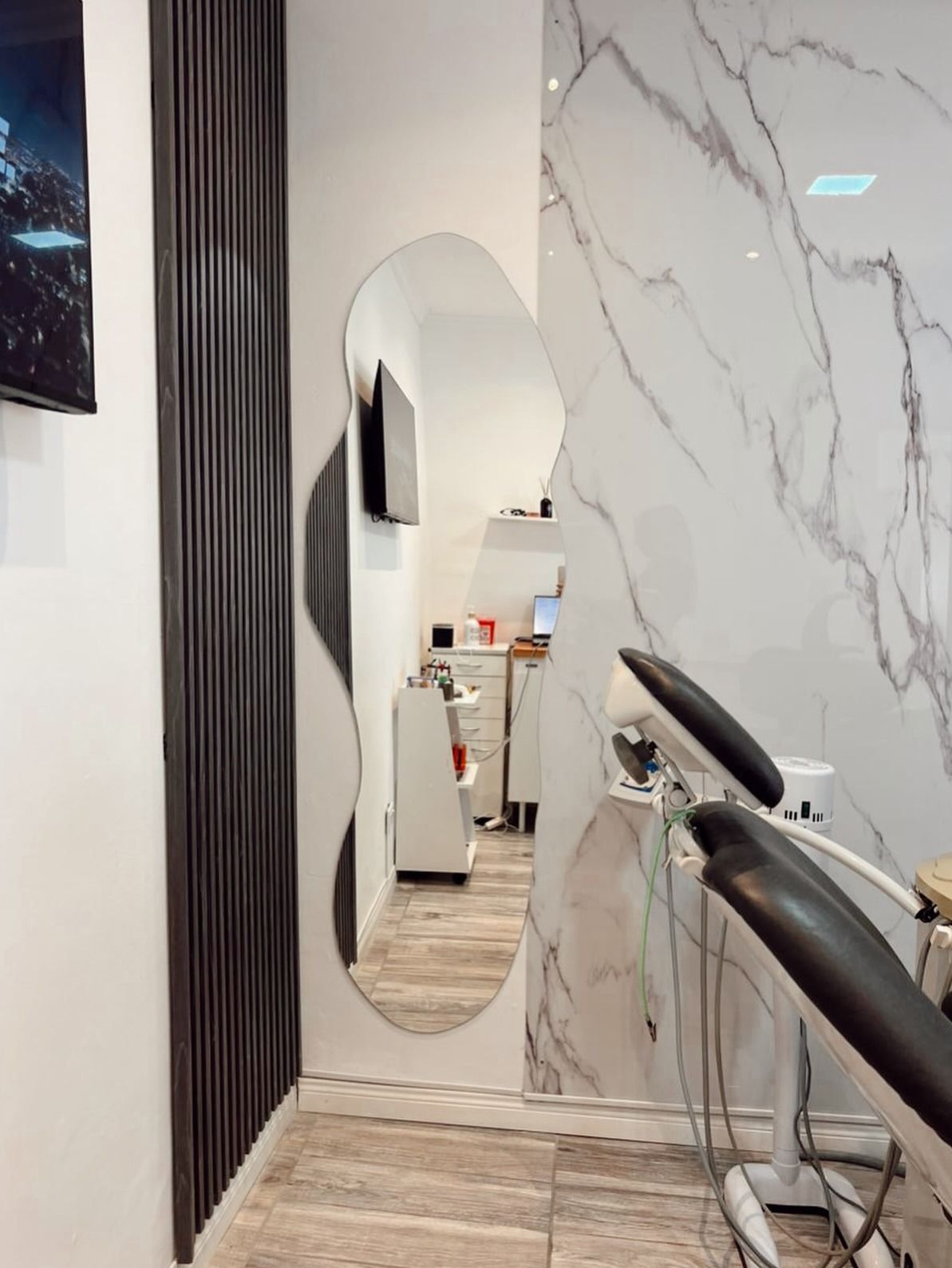 Pasillo interior moderno con pared de mármol, espejo ovalado, cortina a rayas y una silla negra.