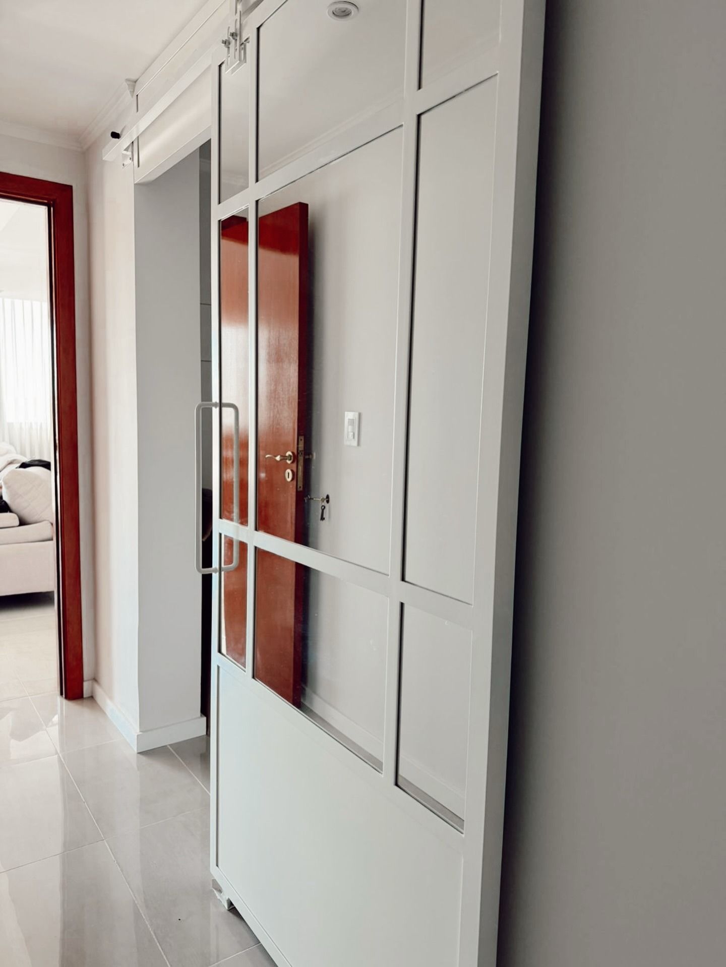 Pasillo blanco con grandes puertas de armario con espejo y una puerta que da a un dormitorio con marco rojo.