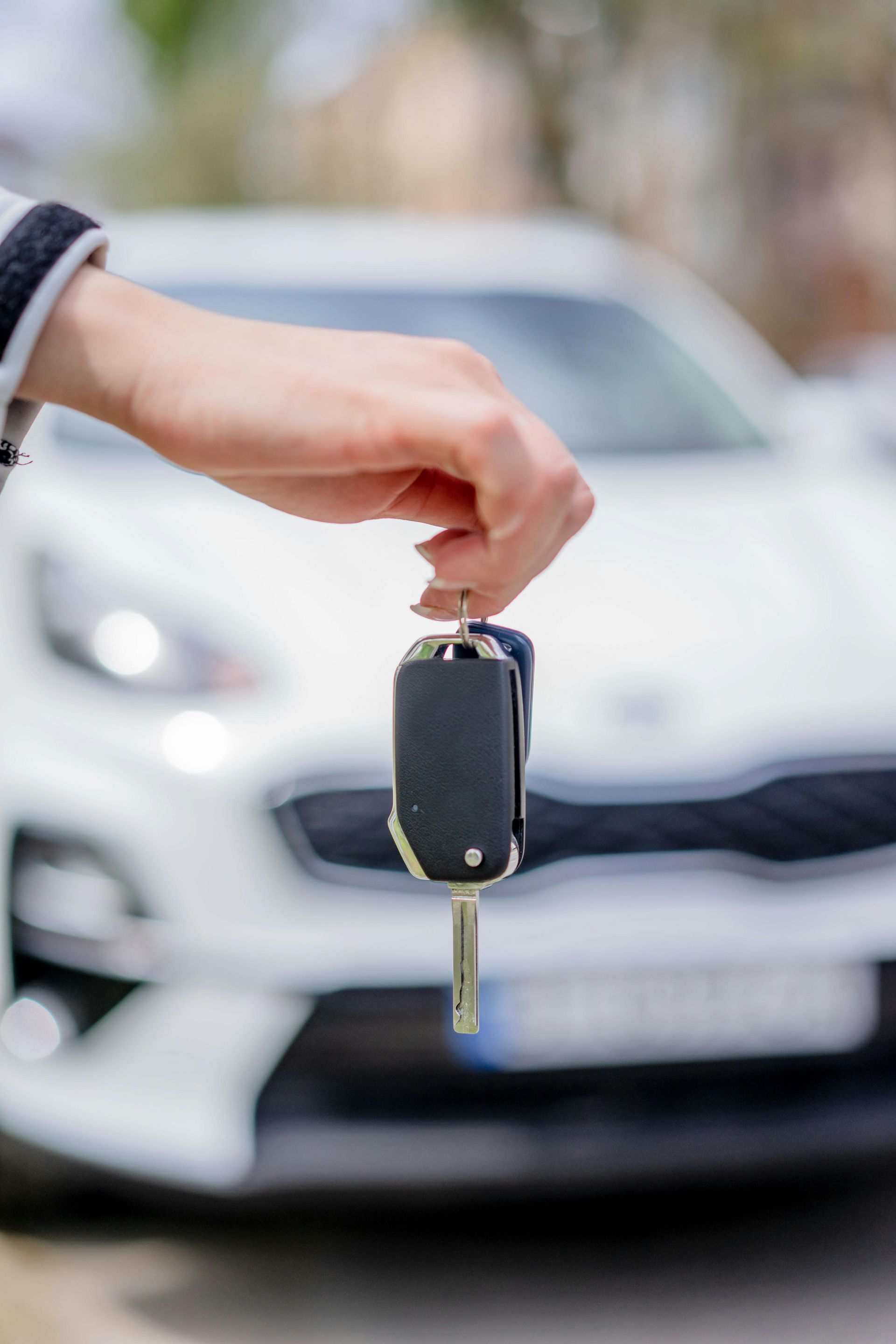 A person is holding a car key in front of a white car.