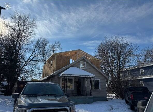 A car is parked in front of a house under construction.