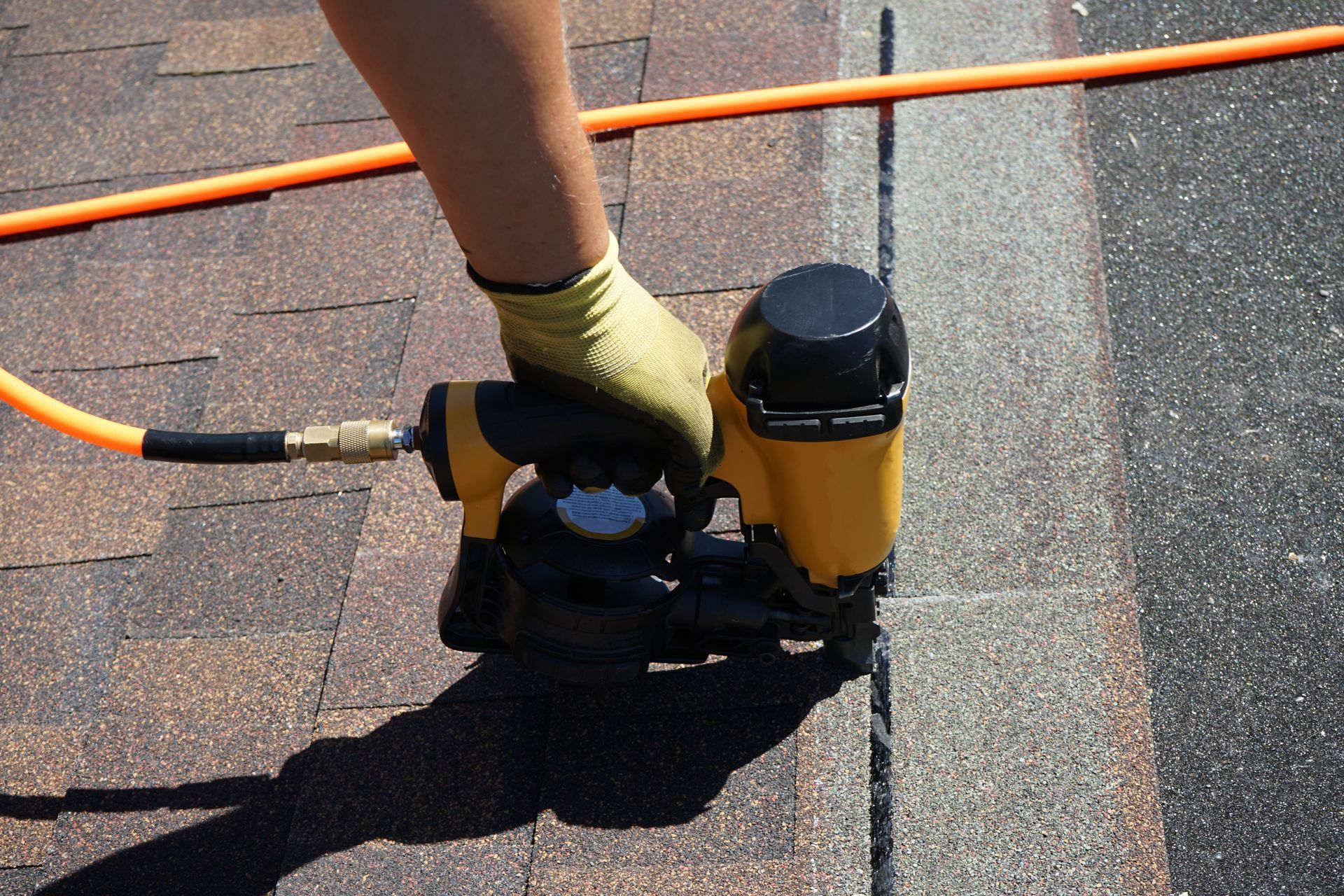 Worker installing shingles with roofing nail gun.
